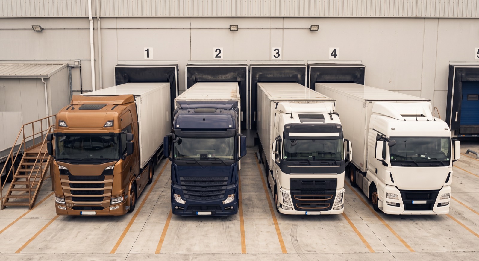 Four trucks backed up to numbered loading docks at a distribution center